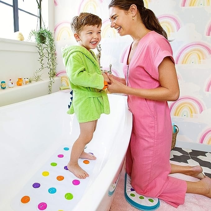 Child stands on a bathmat while a woman helps