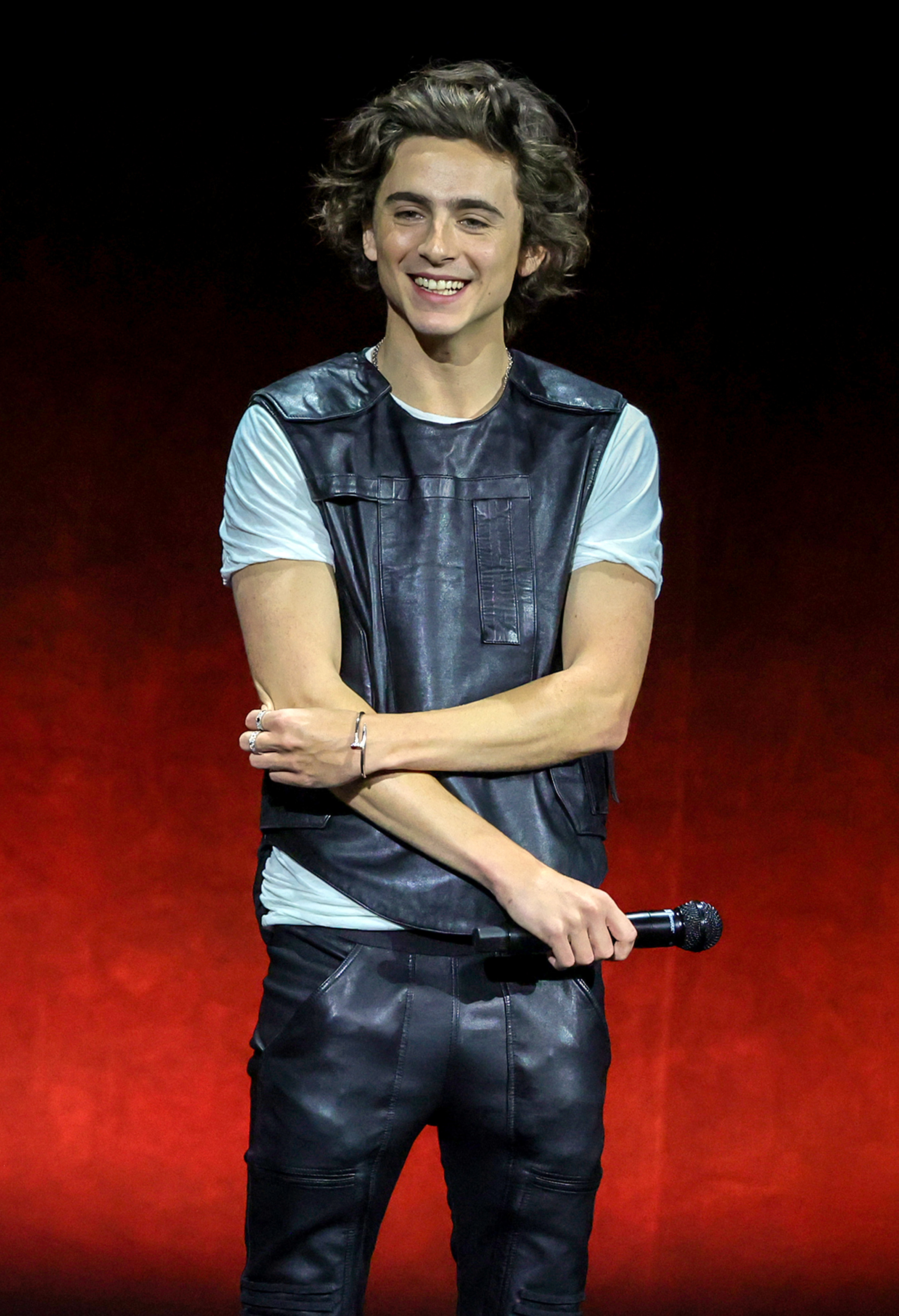 Close-up of Timothée smiling onstage and holding a microphone