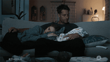 a man holding a small baby while his wife lays on his lap