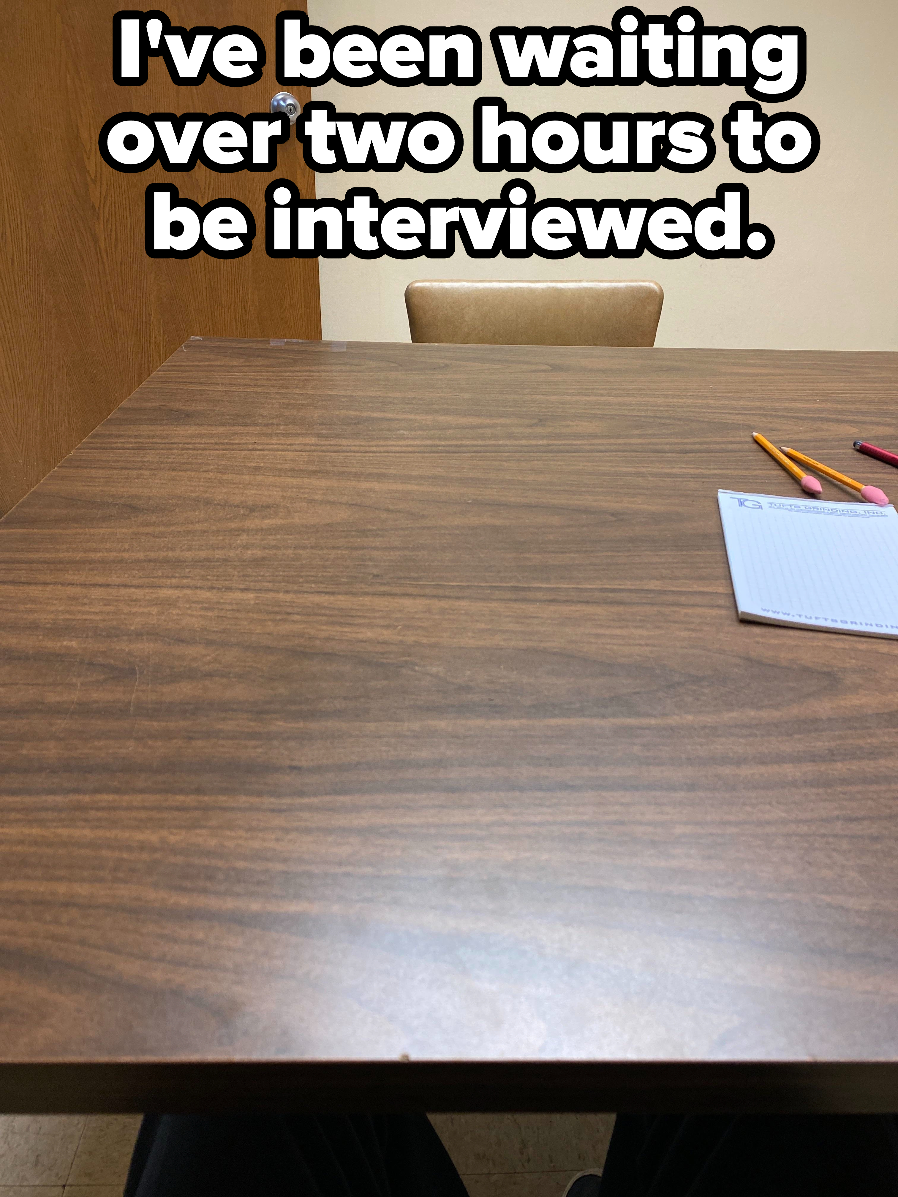 A desk and an empty chair with caption, "I've been waiting over two hours to be interviewed"