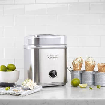 Stainless steel ice cream maker surrounded by ingredients and ice cream in cones
