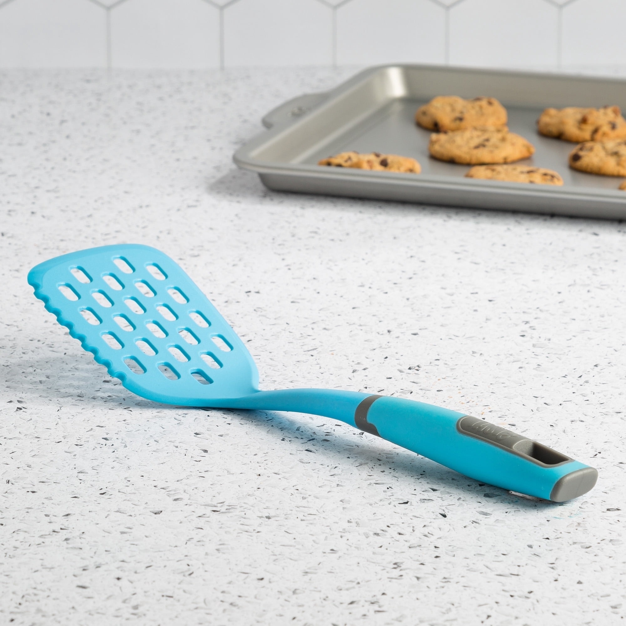 A blue slotted turner on a counter with cookies