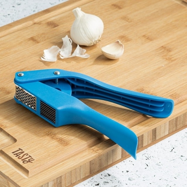 Blue garlic mincer on a wood cutting board with garlic.