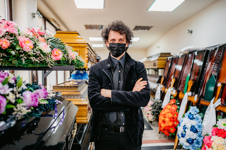 guy wearing a face mask in a parlor filled with coffins
