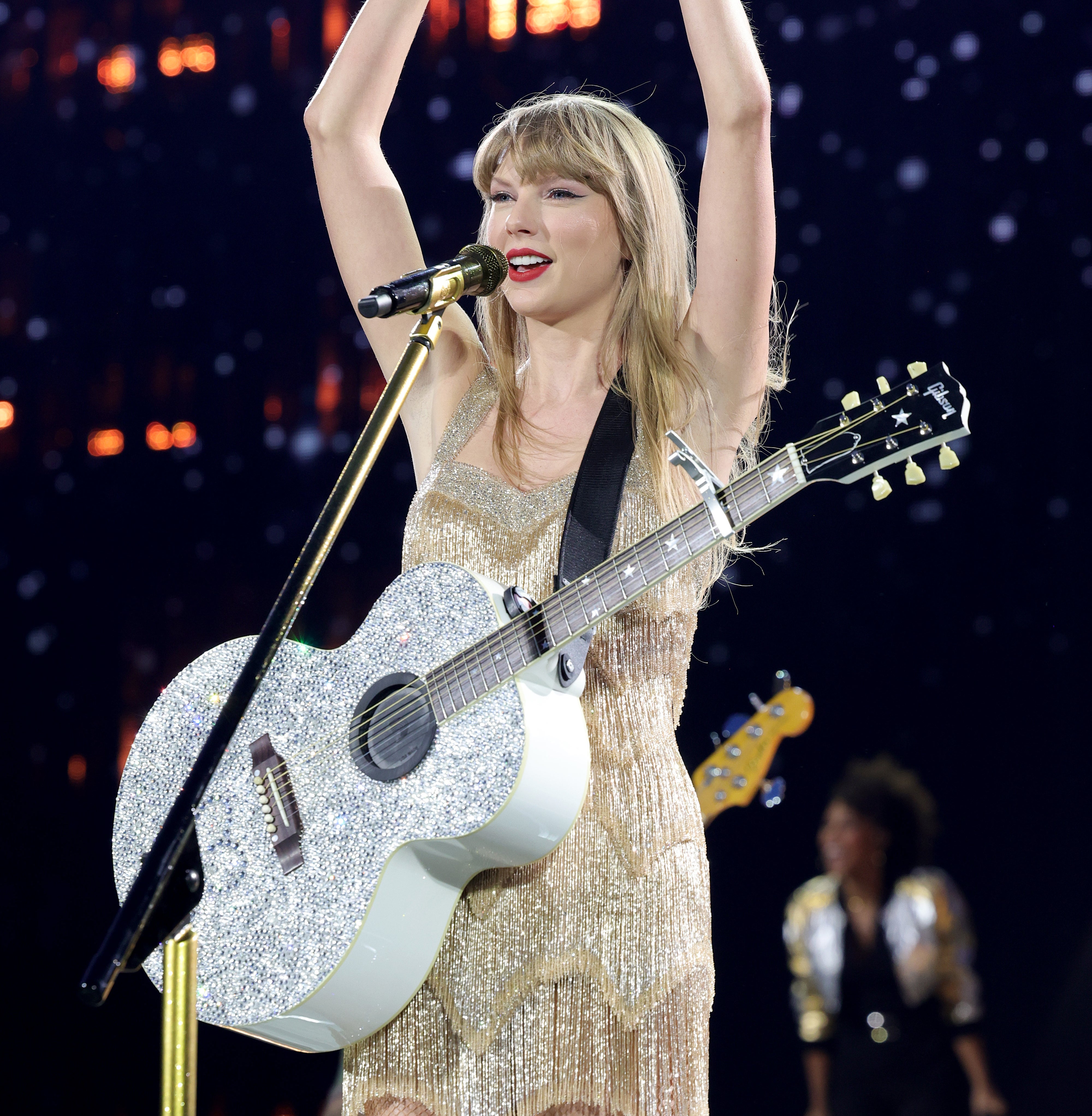 Taylor Swift at a concert, holding her arms aloft to form a heart with her hands