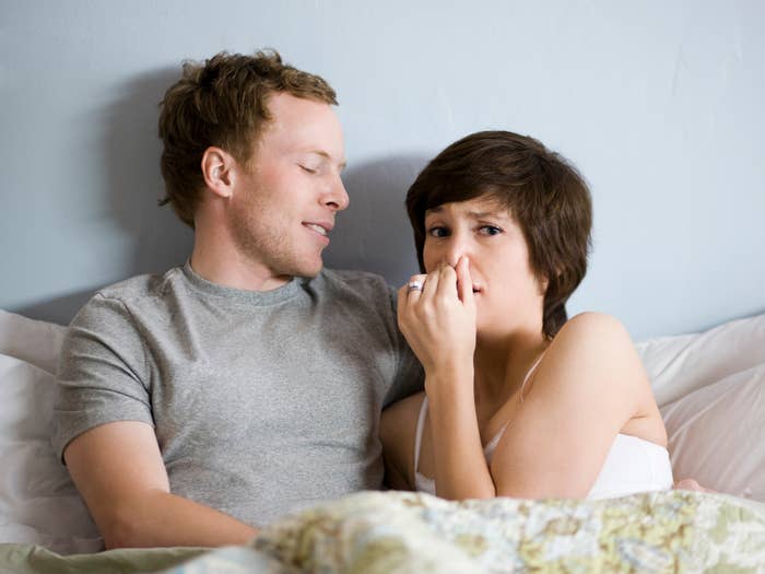 A woman plugging her nose while in bed with her partner
