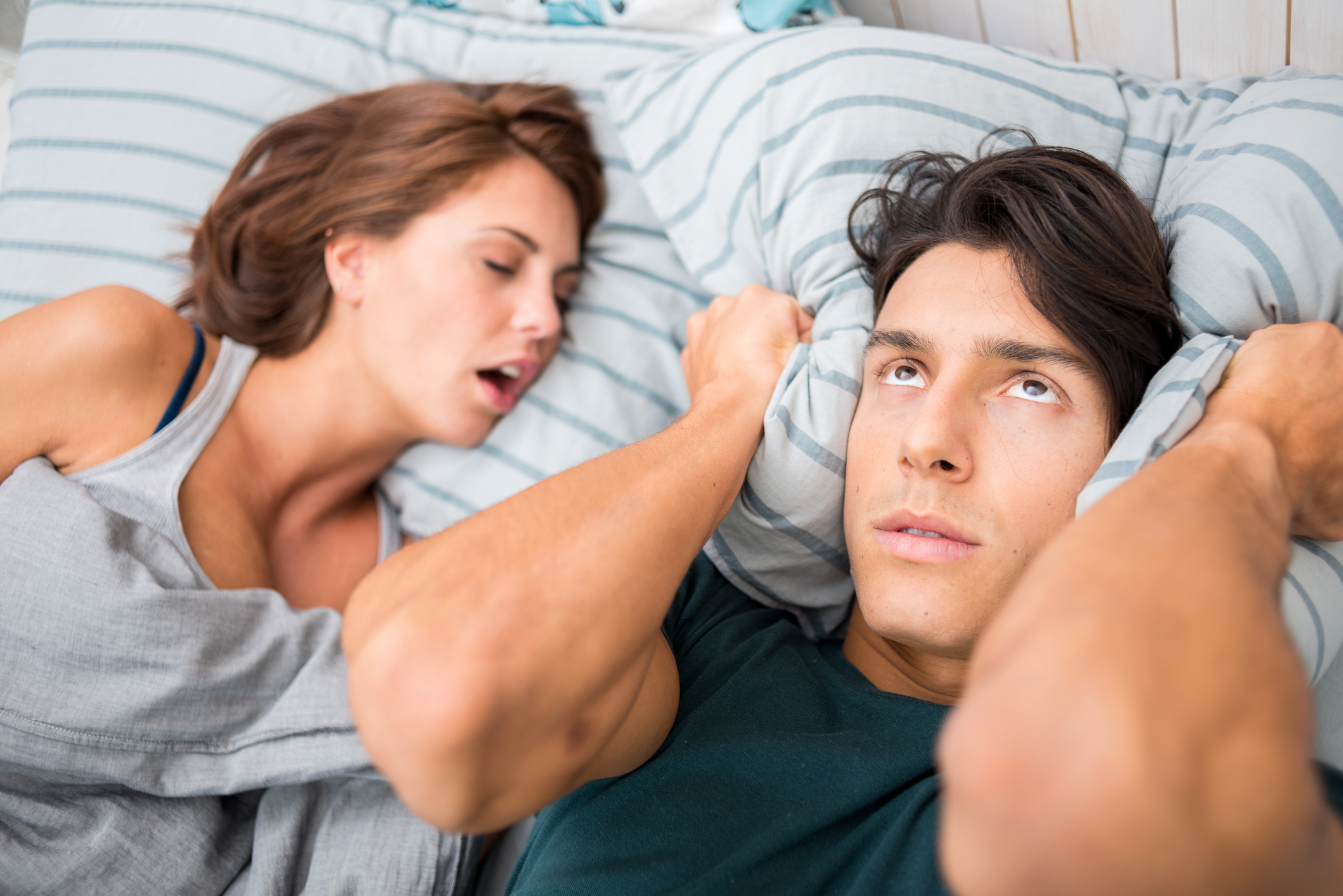 A man covering his ears with his pillow while his partner sleeps next to him