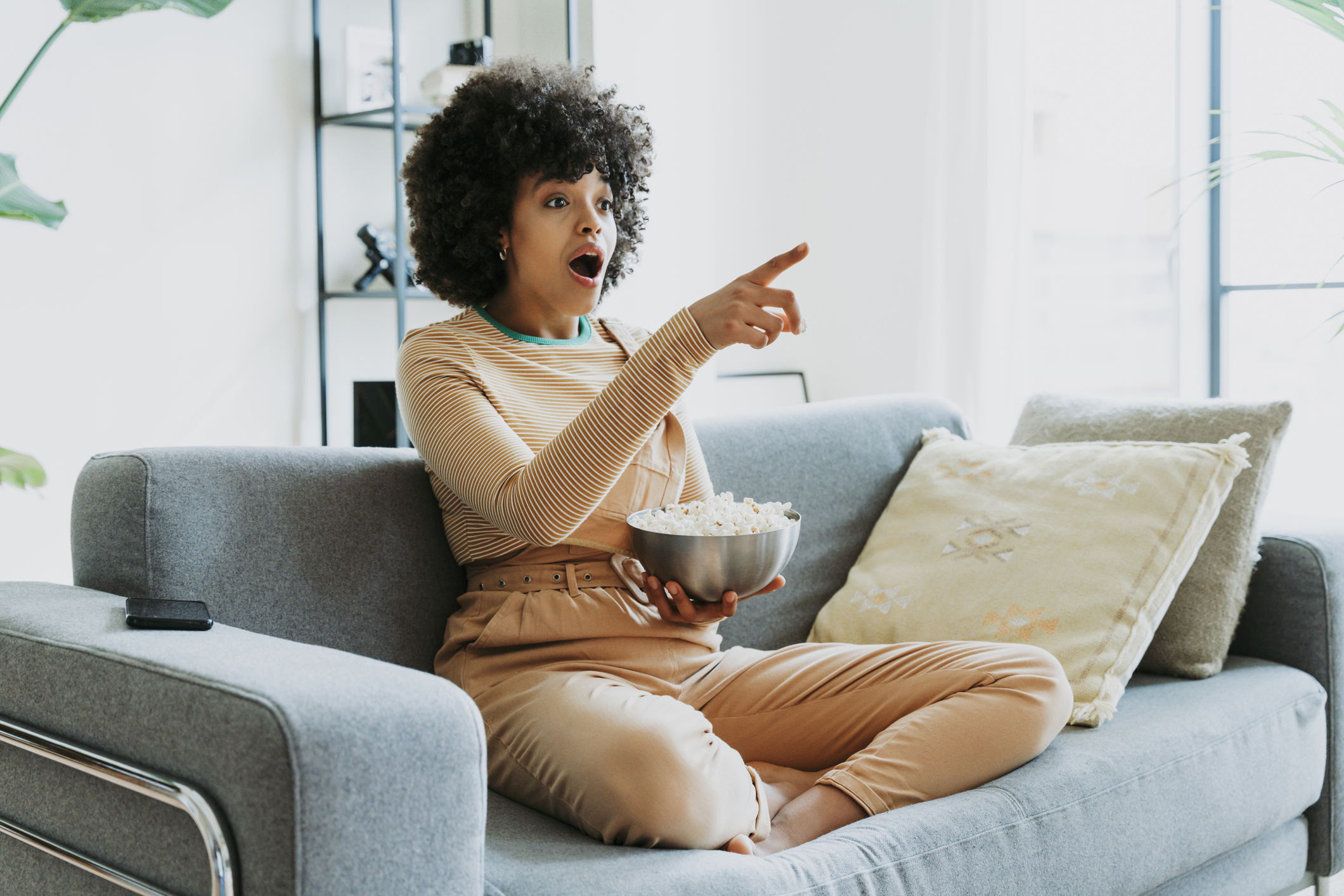 A woman eating popcorn and pointing to the TV