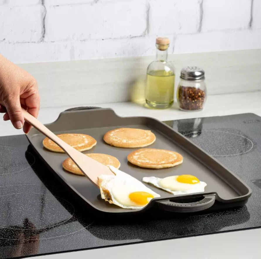 flat griddle pan on stove with four small pancakes and sunny side up eggs
