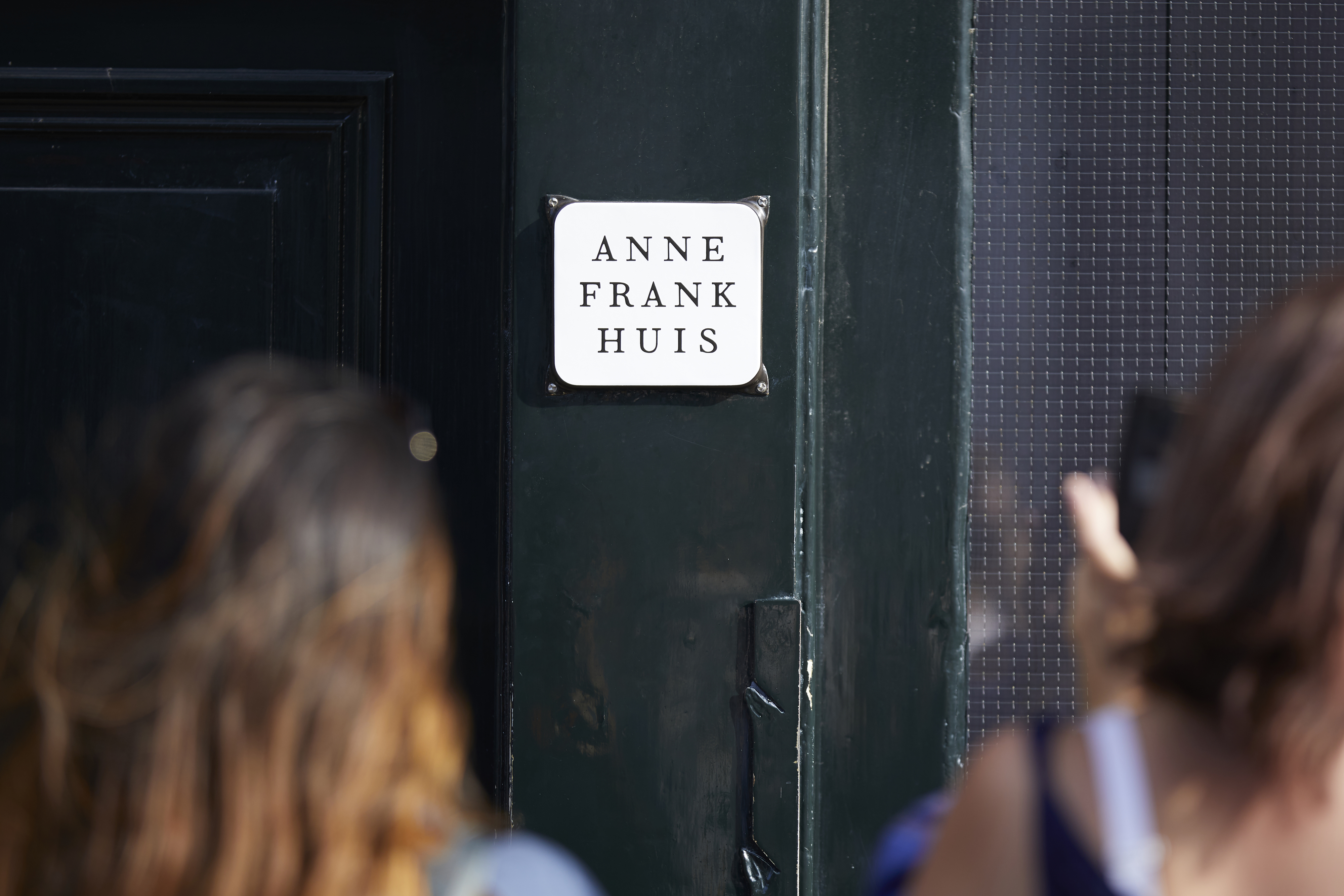 People standing outside a building that has a plaque with the words &quot;Anne Frank Huis&quot; on it