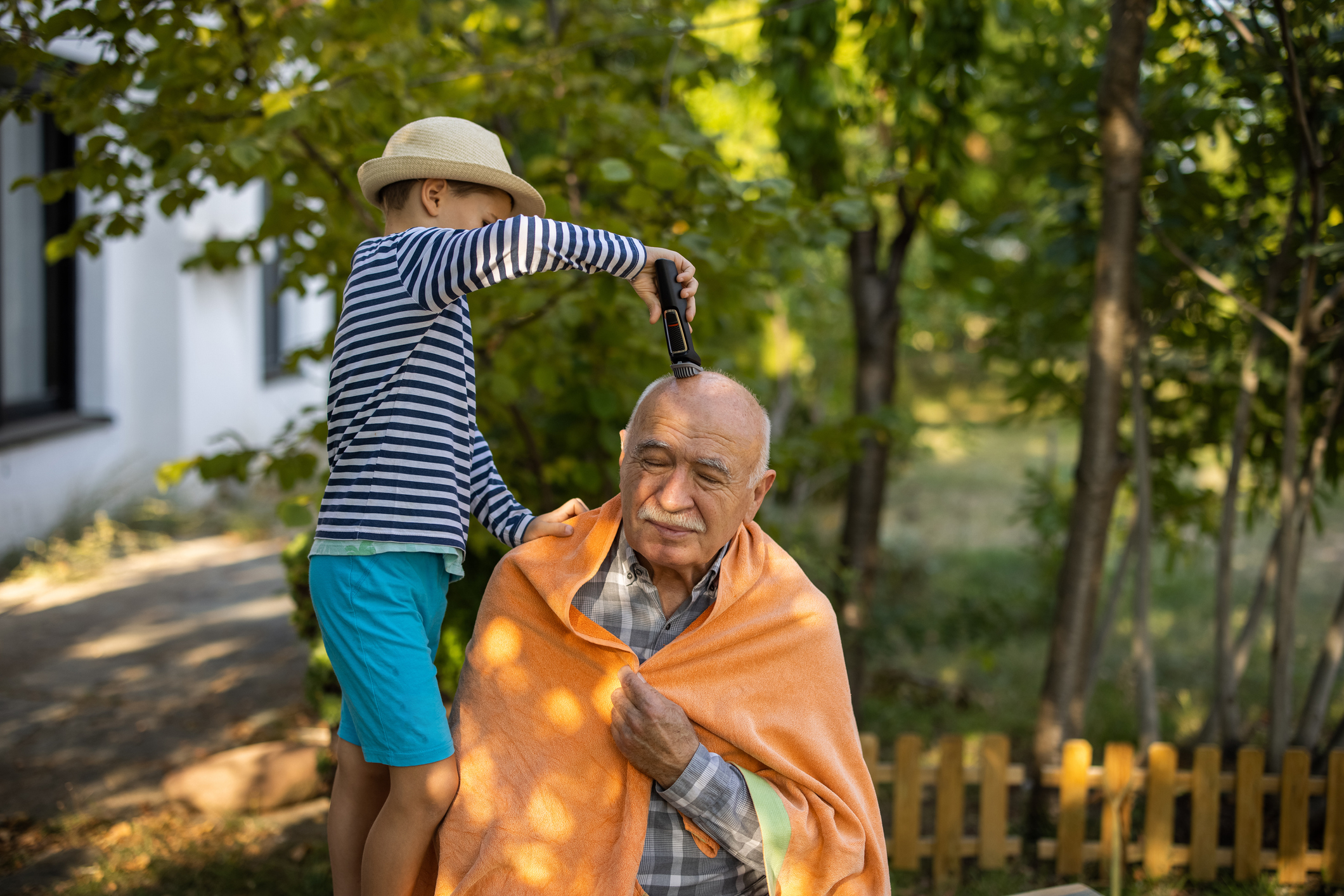 A child is shaving his grandpa&#x27;s head