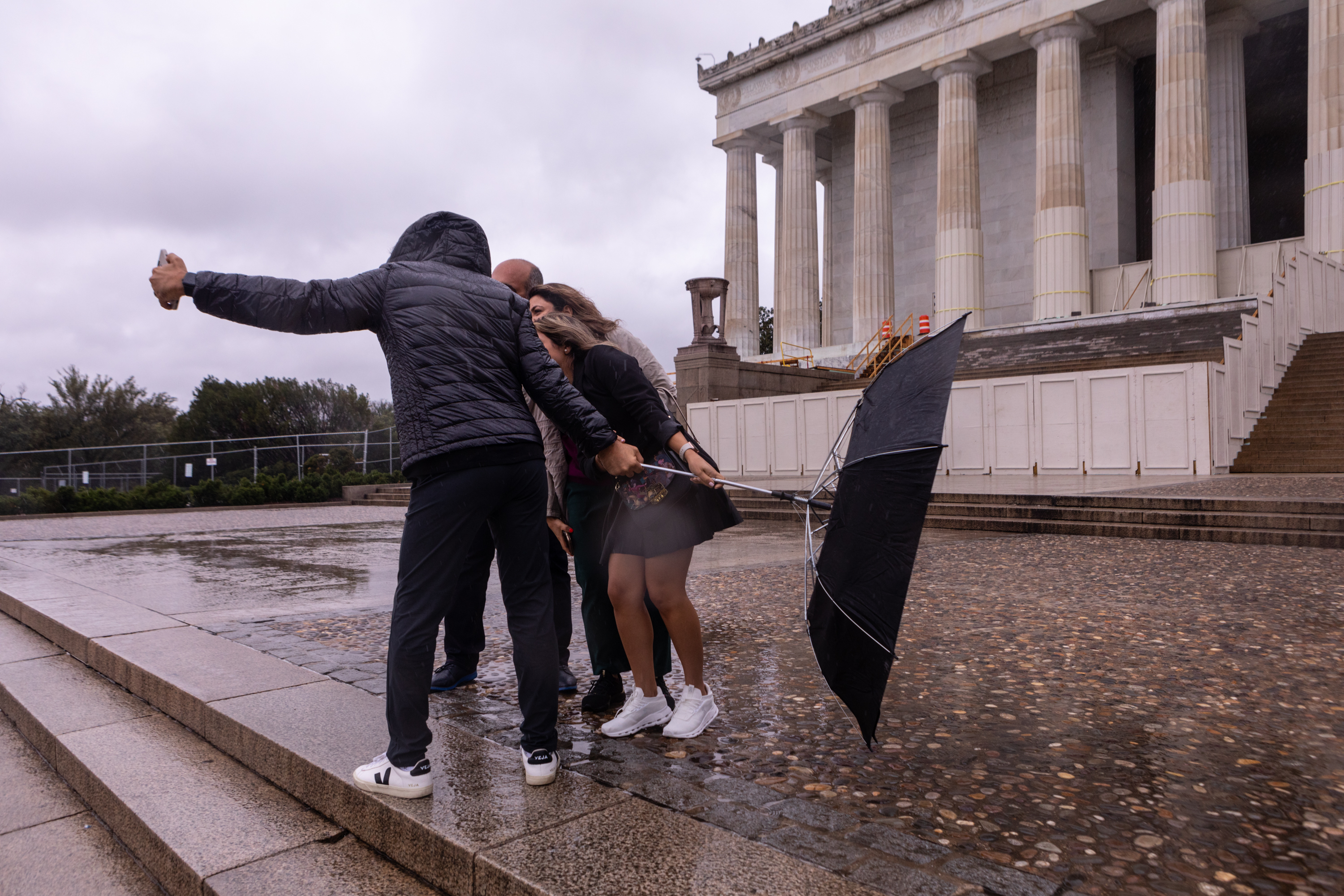 People struggling to hold onto an umbrella as they try to take a photo at the Lincoln Memorial