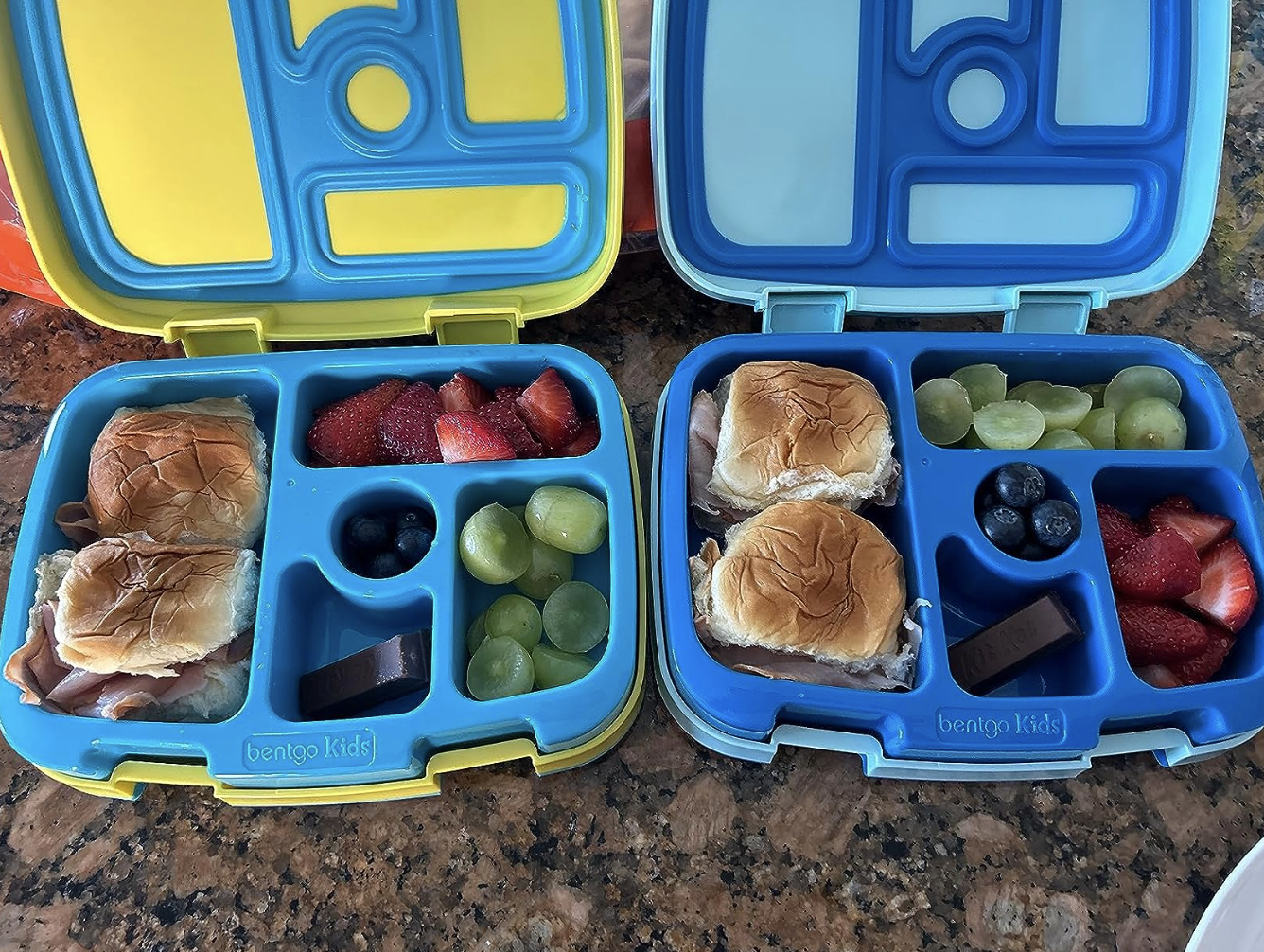 two lunch boxes with various foods in each compartment