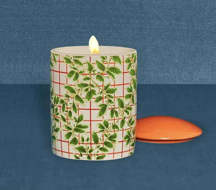 Lit L'or de Seraphine candle with a plaid red and leaf-print design
