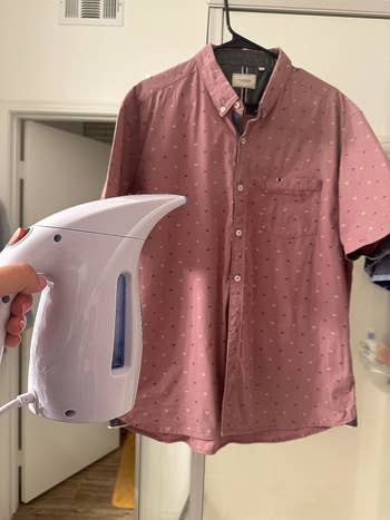 a reviewer holding a steamer in front of a wrinkle-free shirt 