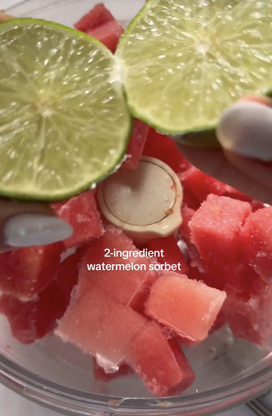 Frozen watermelon chunks in a food processor and hands squeezing a lime into the bowl