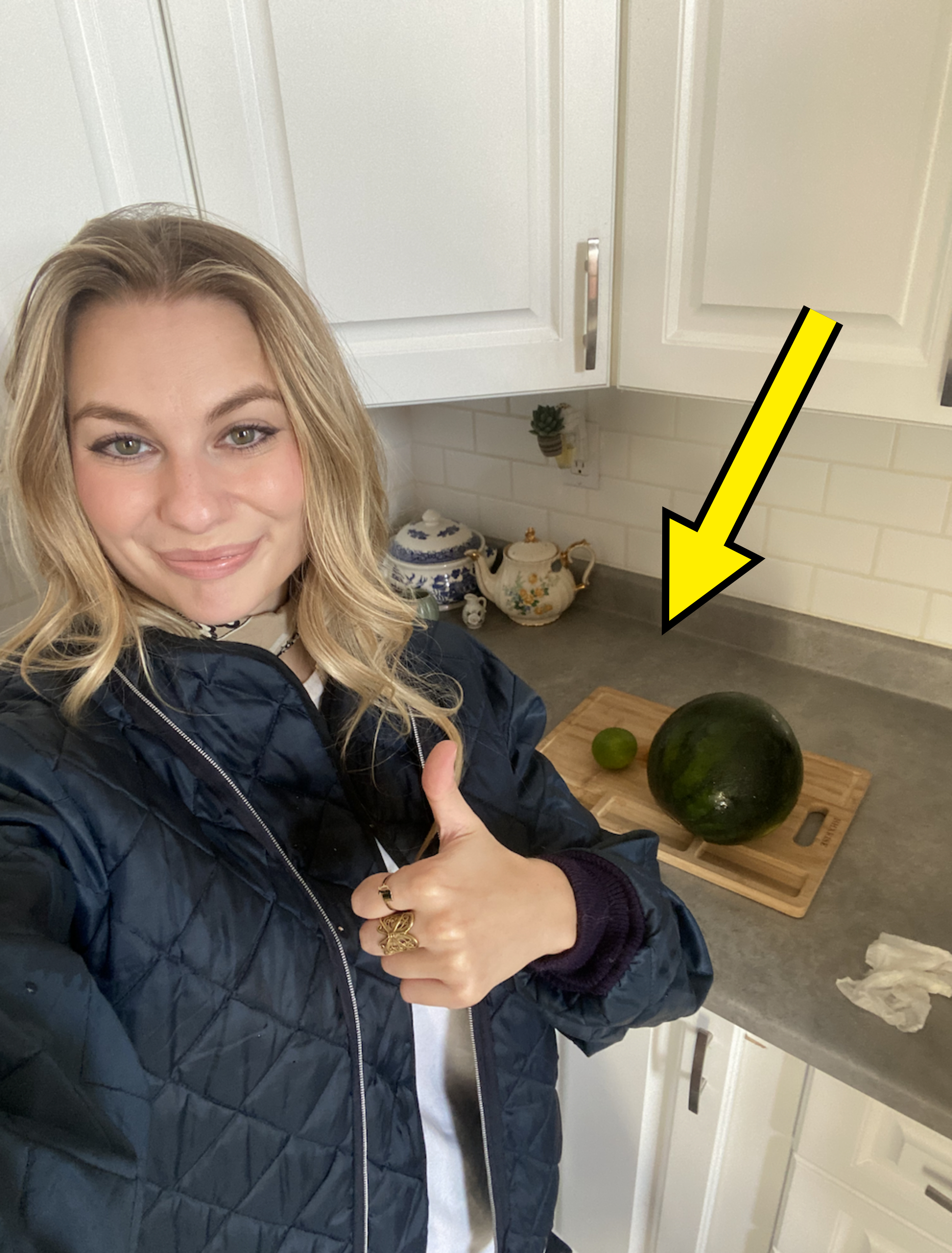 Me smiling with my thumb up standing in my kitchen next to a cutting board that has a watermelon and lime sitting on it