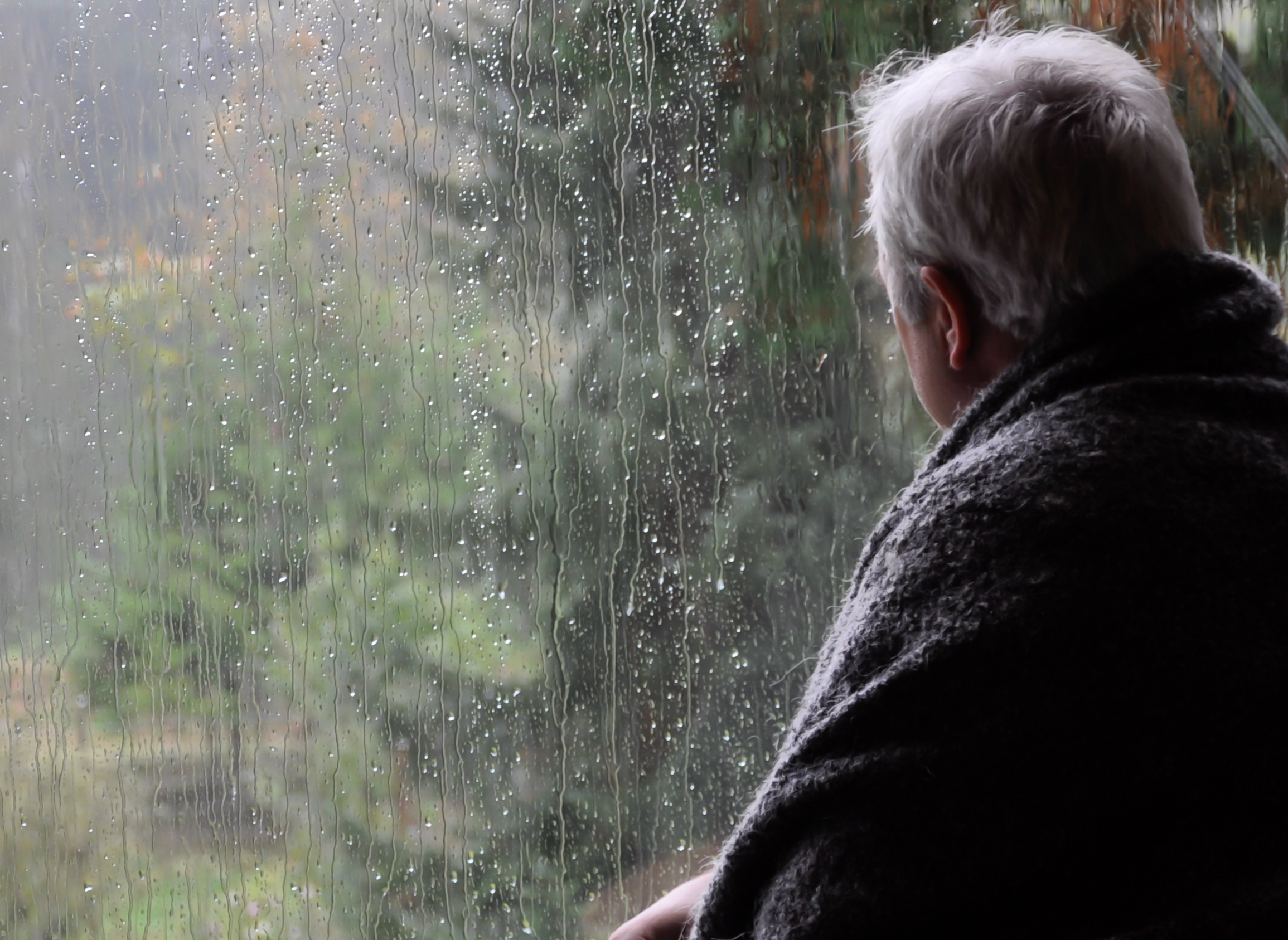 lonely gray haired man looking out the window on a rainy day