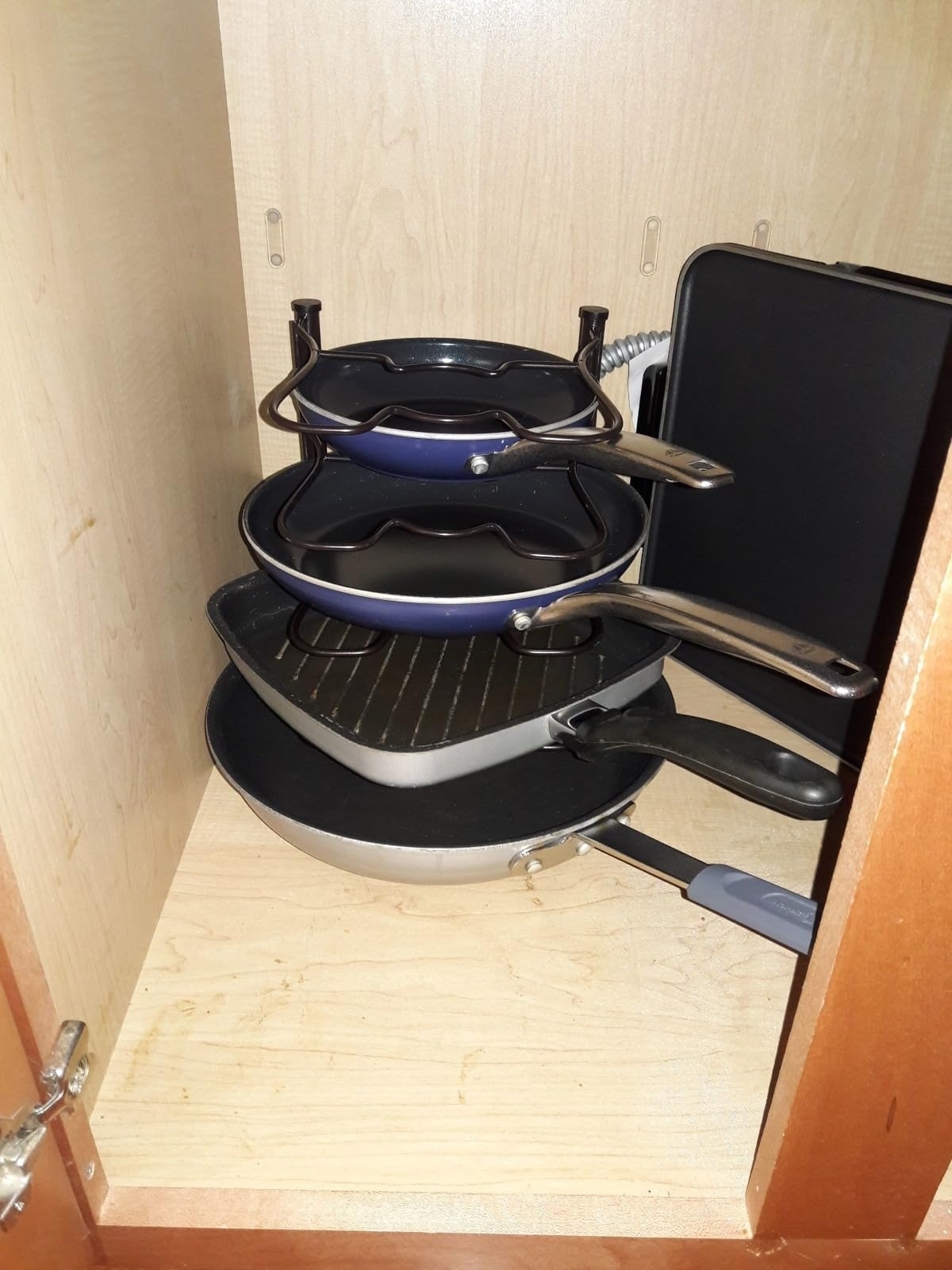 black pan organizer with dark blue and silver skillets in an open cabinet