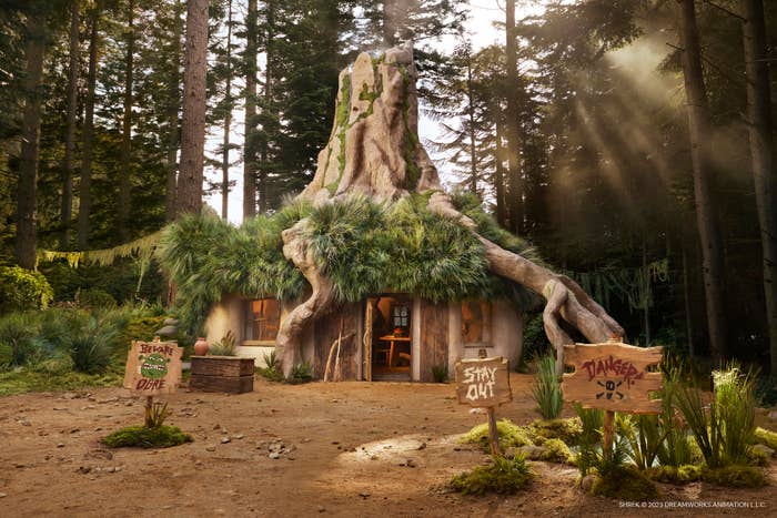 Fantasy cottage resembling a tree trunk with a door, surrounded by forest and sunlight, with &quot;Stay Out&quot; signs