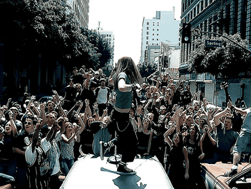 Avril Lavigne sings on top of a car in a crowded intersection.