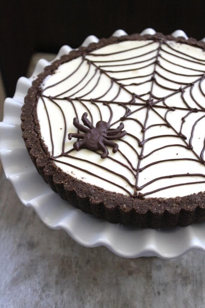 a cheesecake with a dark tart crust and a spider web pattern and spider piped on top
