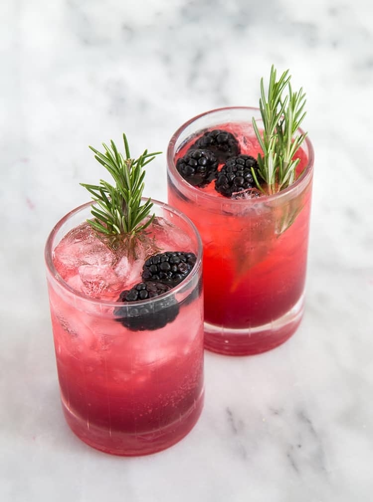two glasses of rosemary blackberry limonata garnished with blackberries and a sprig of rosemary
