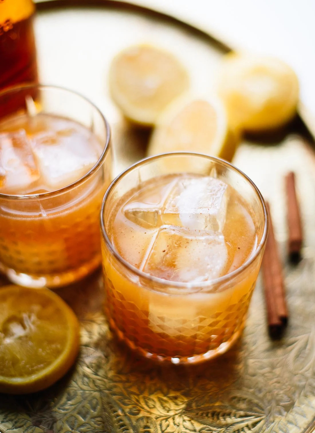cinnamon maple whiskey sour in a glass surrounded by lemons and cinnamon sticks