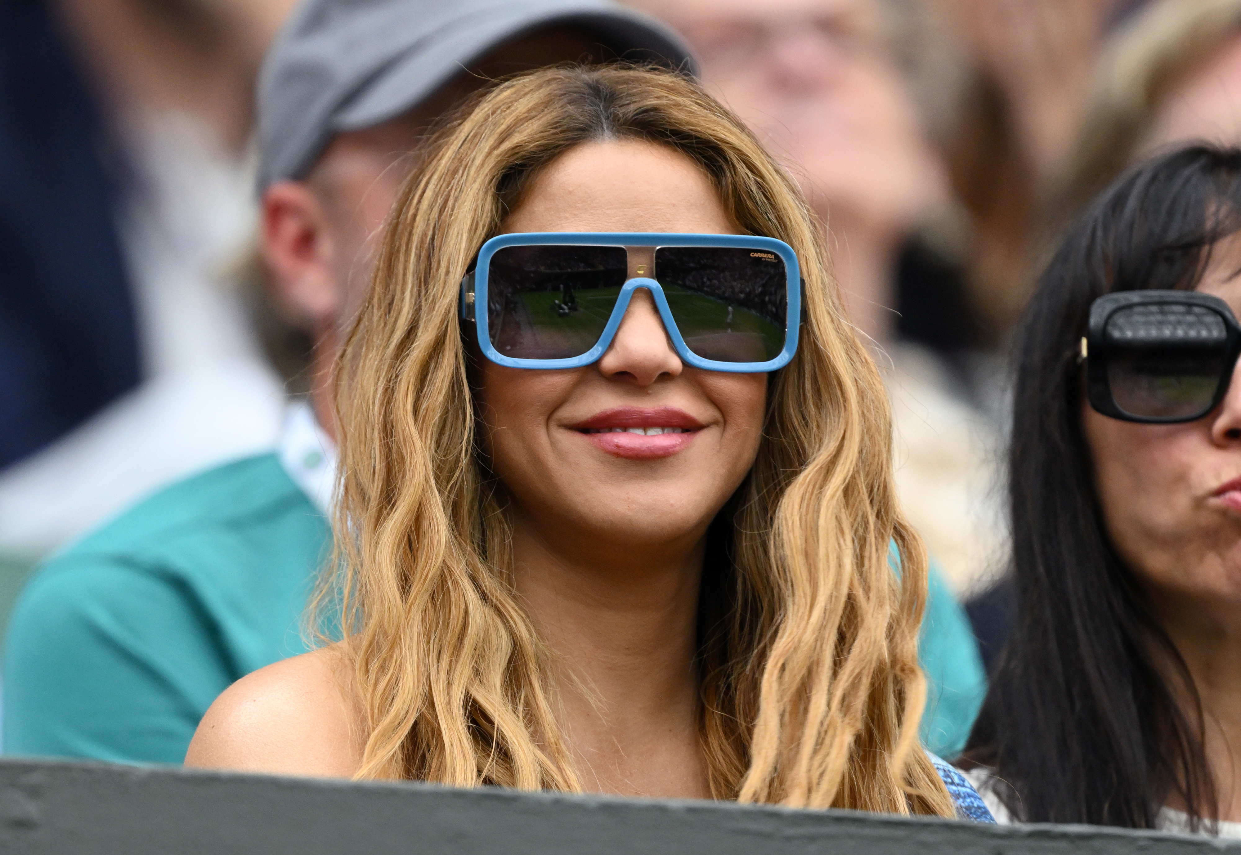 Closeup of Shakira sitting at an outdoor event with sunglasses