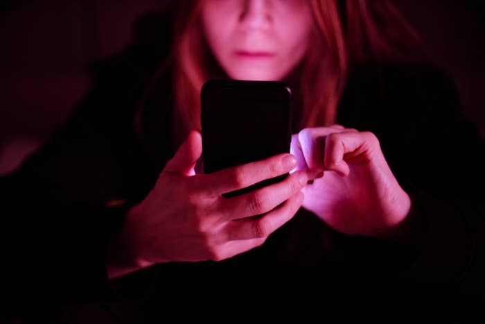 A person staring at their glowing phone screen in a dark room