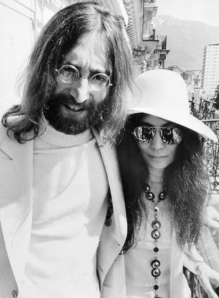 john wearing his signature circular glasses and yoko wearing sunglasses with a floppy hat