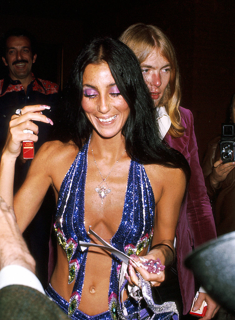 cher in a sparkly outfit with cutouts along the stomach and gregg behind her in a velvet jacket