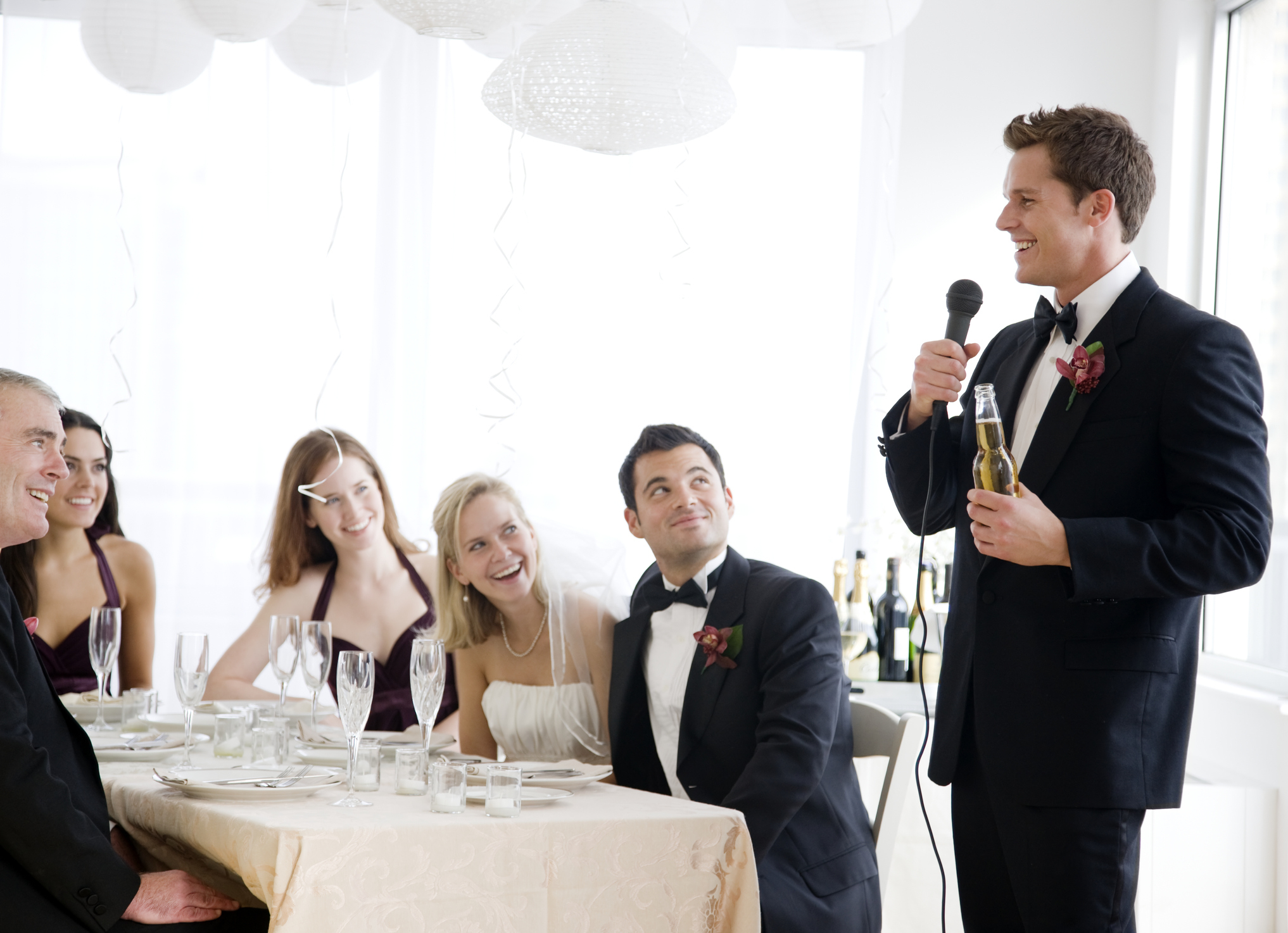 A best man giving a speech at a wedding with a beer and microphone in his hands