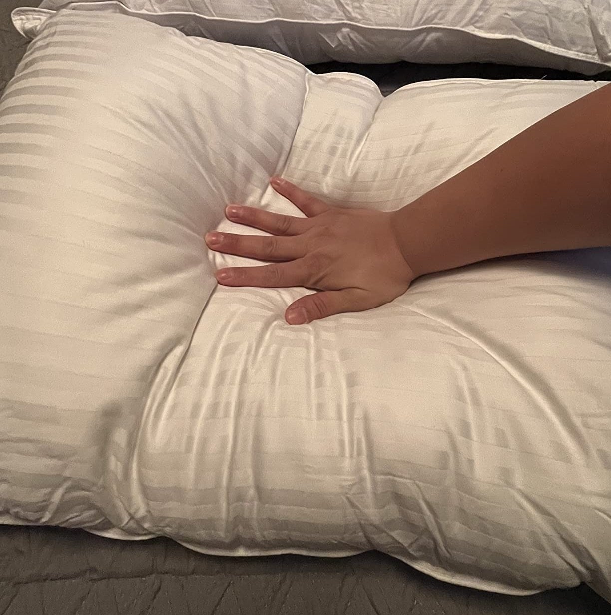 a reviewer&#x27;s hand pressing into the white pillow