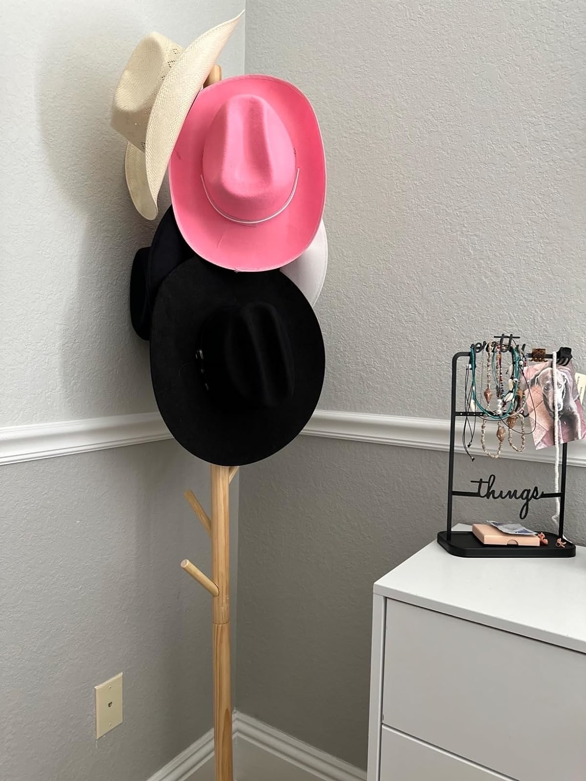 Reviewer image of the light wood coat rack with hats hanging on it in the corner of a room