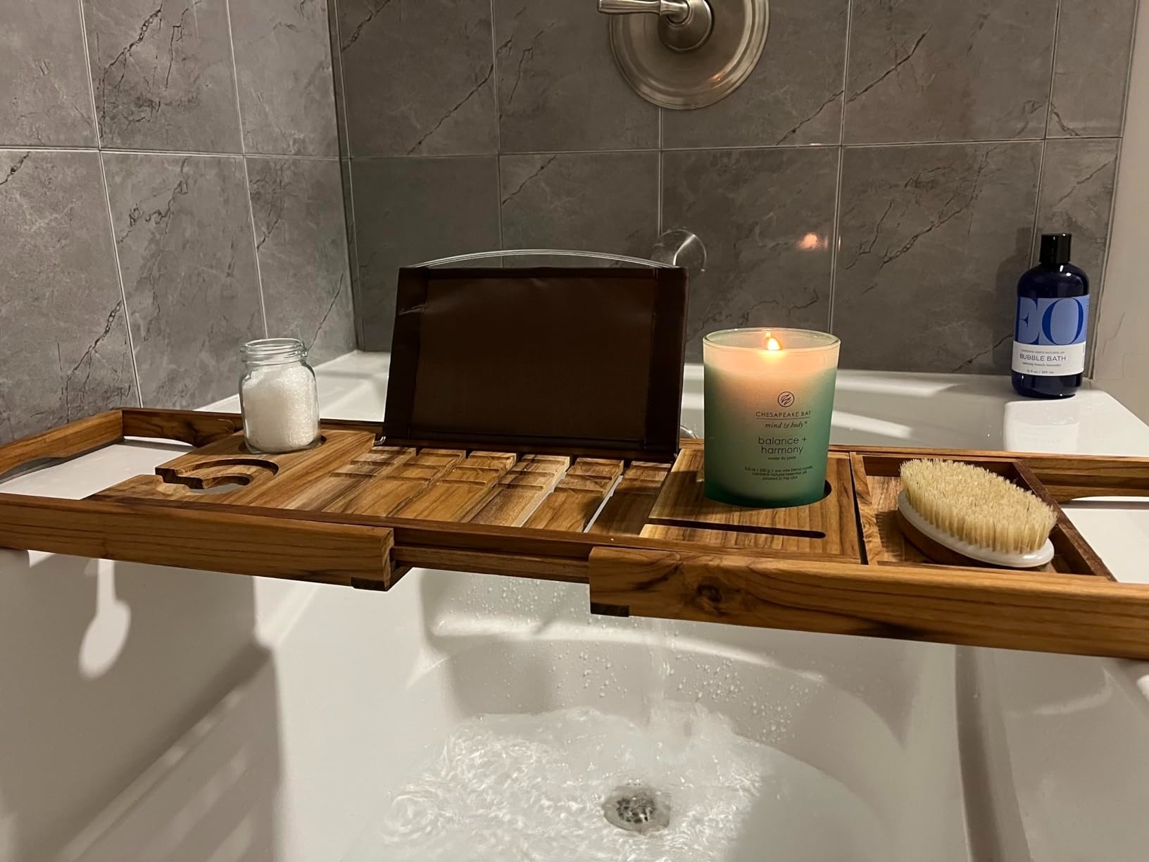 a reviewer photo of the teak wood bathtub tray with a tablet, candle and bath accessories