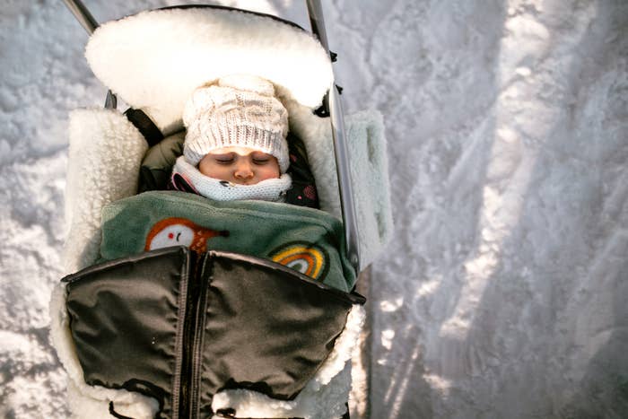 A baby is sleeping in a stroller outside in the snow