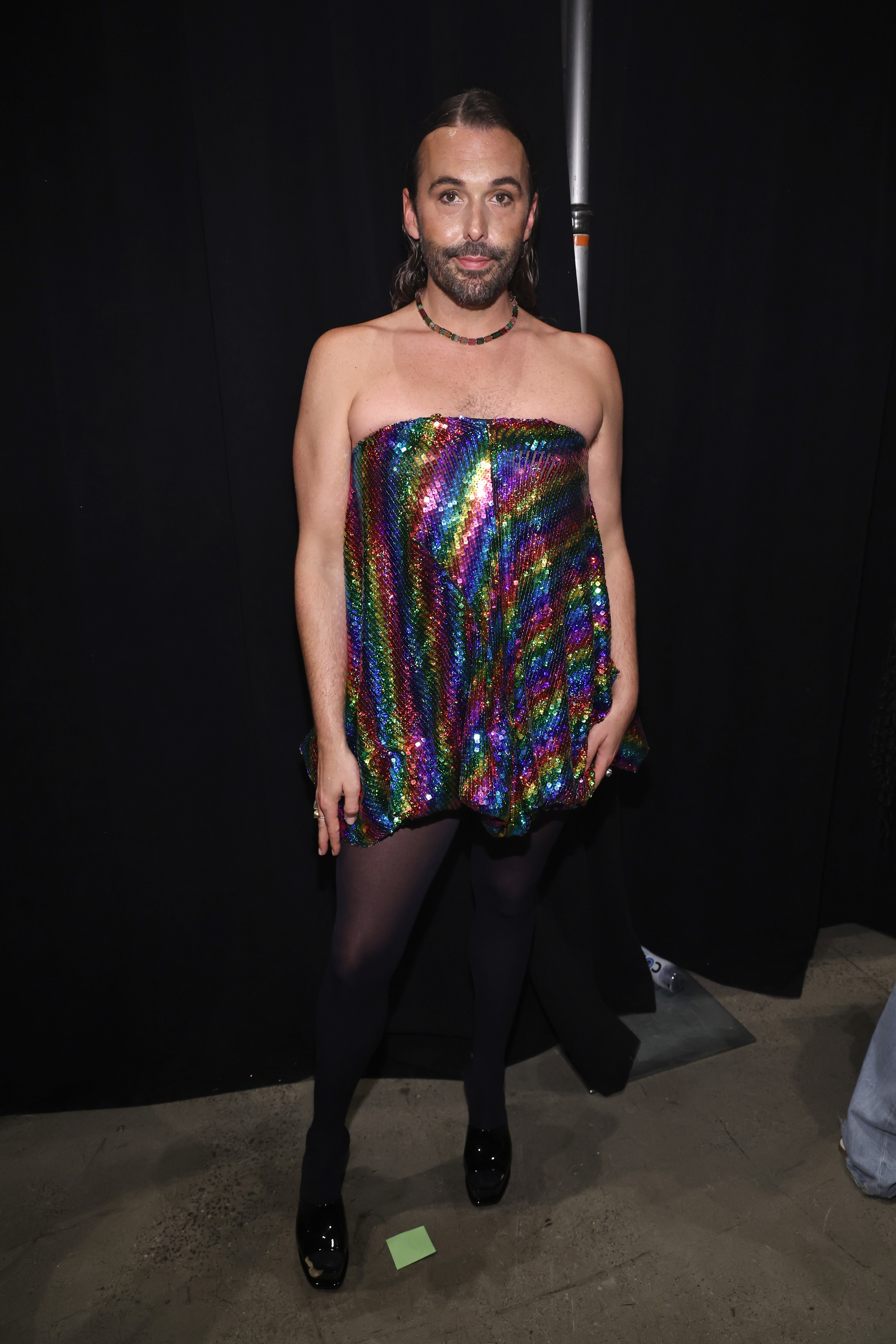 Closeup of Jonathan Van Ness at an event posing for the camera in a sequin strapless dress and tights