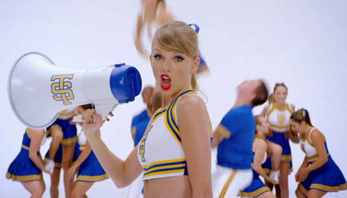Taylor in a cheerleader costume, singing into a megaphone, in the &quot;Shake It Off&quot; video.