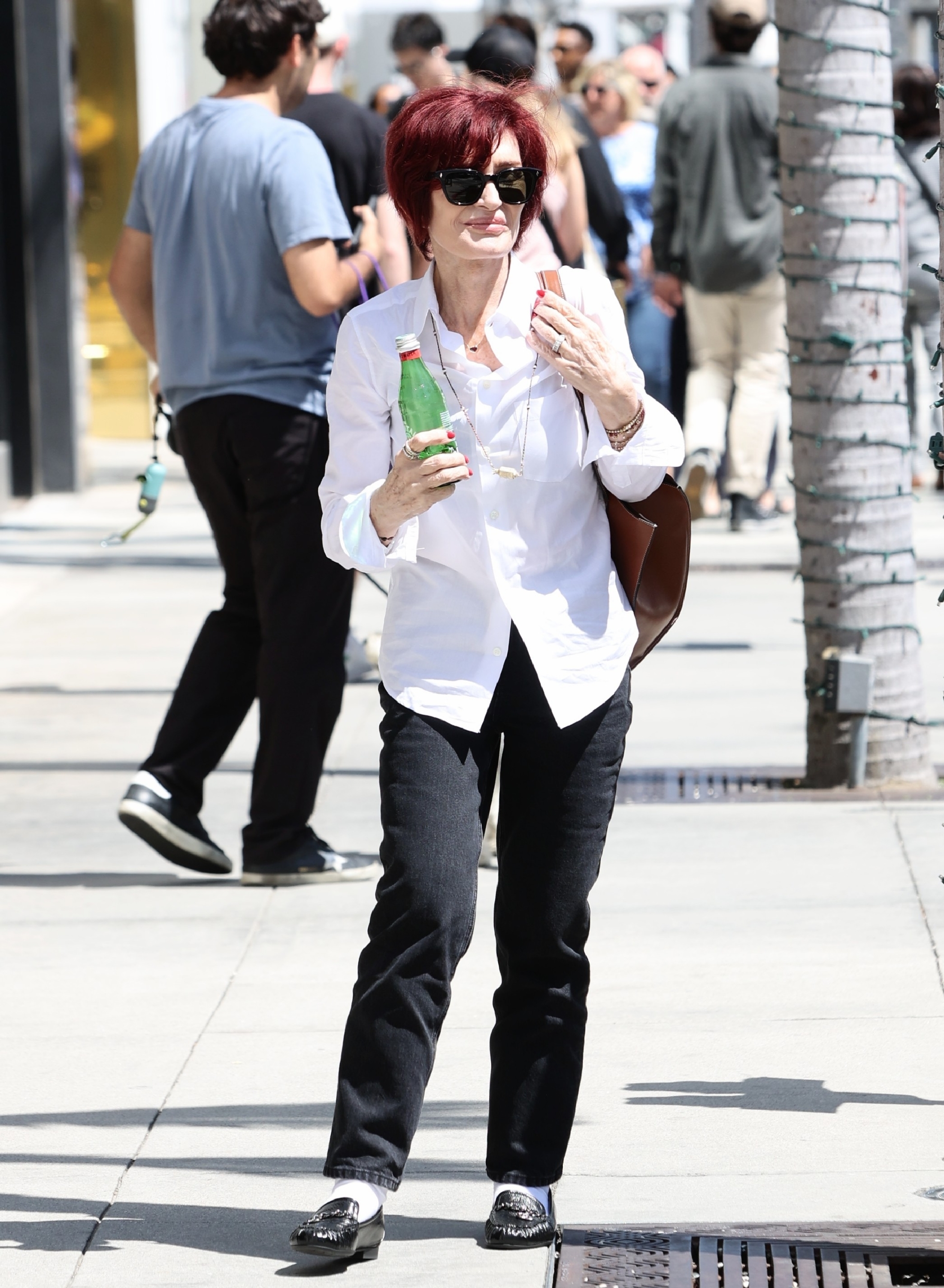 Close-up of Sharon on the street in a shirt and pants and holding a beverage