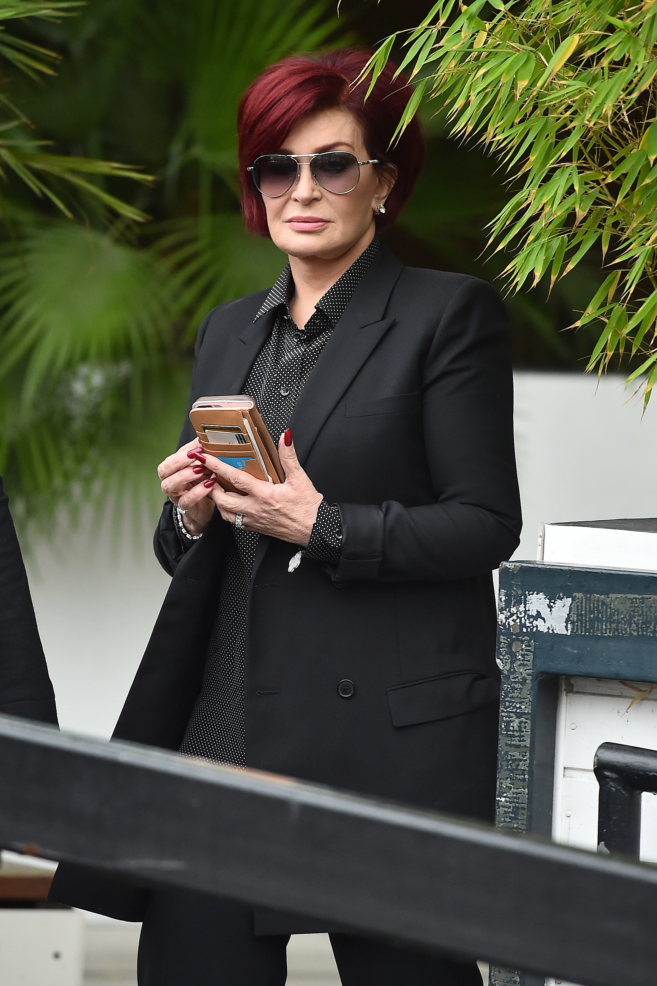 Close-up of Sharon holding a phone and wearing a coat with a verdant background