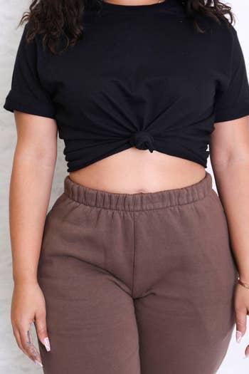 close-up of model wearing black knotted crop tee with brown sweatpants