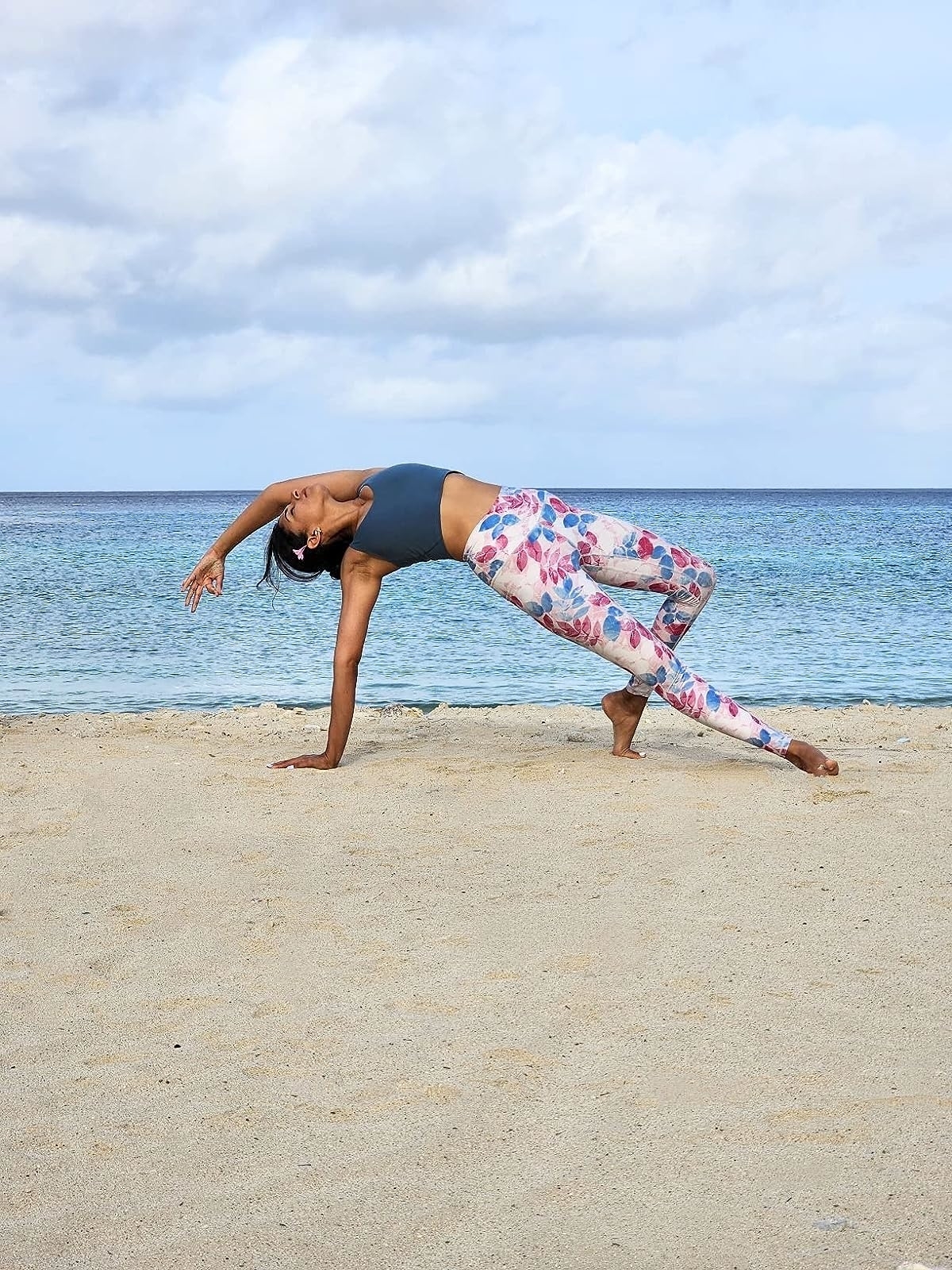 Reviewer wearing the patterned leggings and blue top doing yoga on the beach