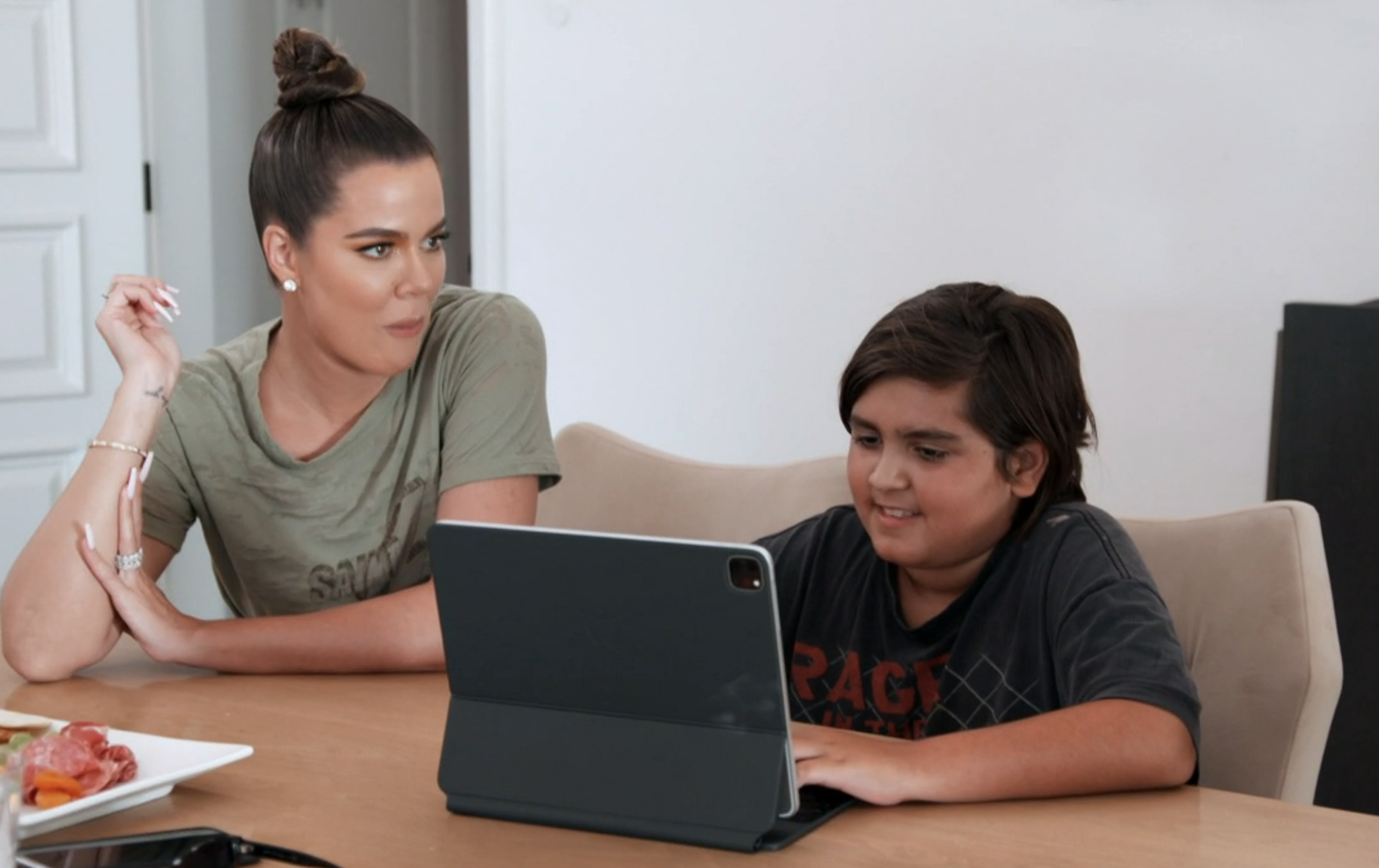 Khloé and Mason sitting at a table in front of a tablet