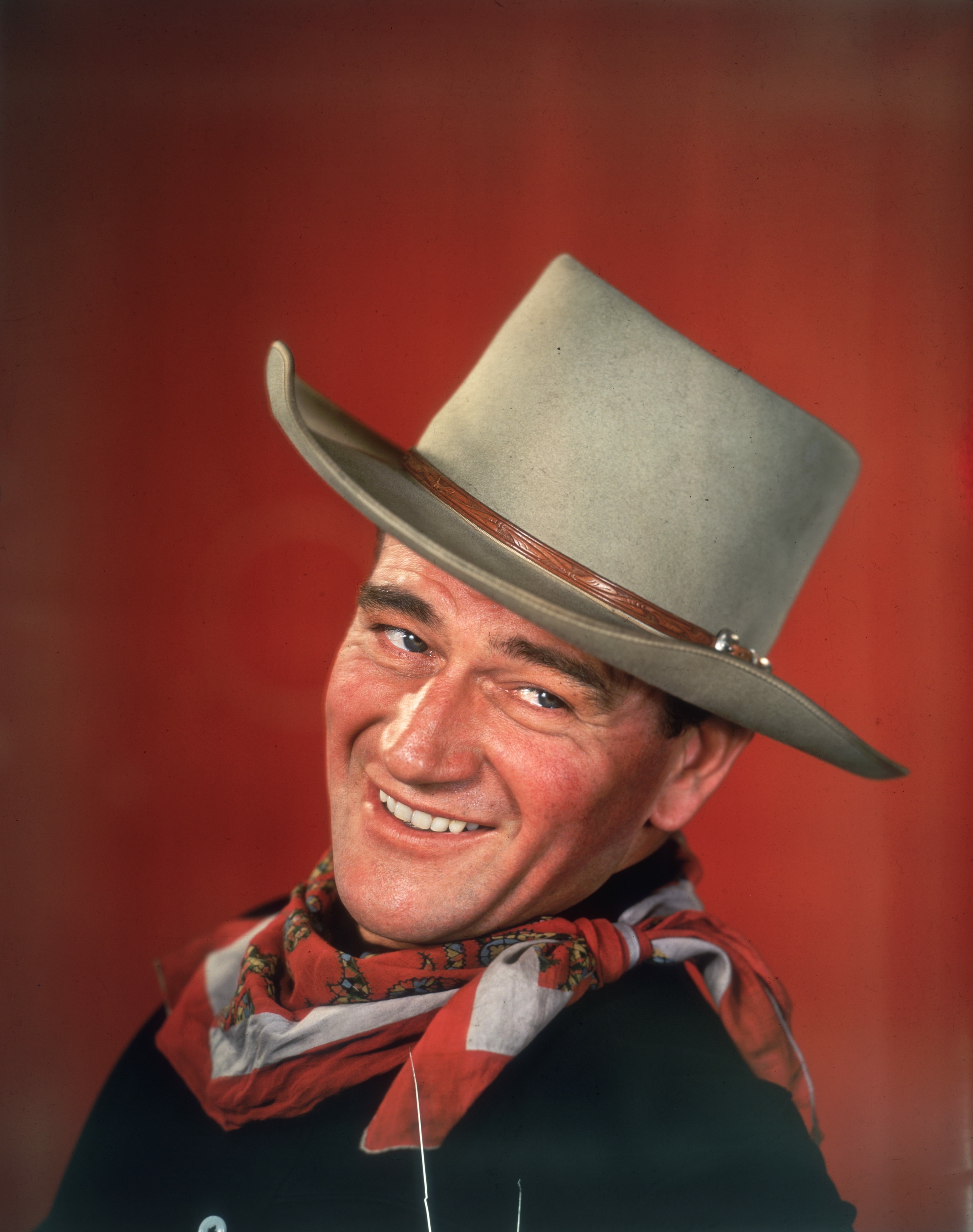 Close-up of John Wayne smiling and wearing a Western hat and scarf around his neck
