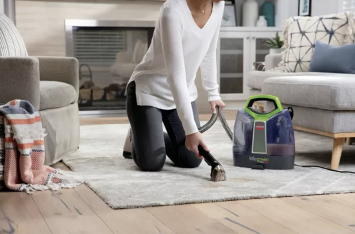 a person kneeling to use a portable carpet cleaner on an area rug