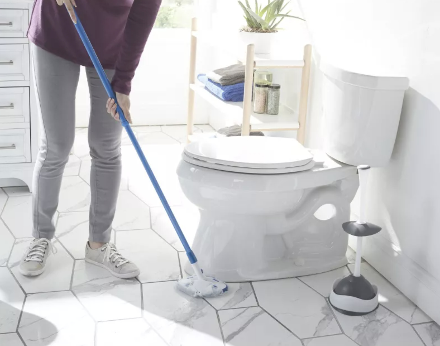 a person using an extending pole scrubber to clean the area under a commode