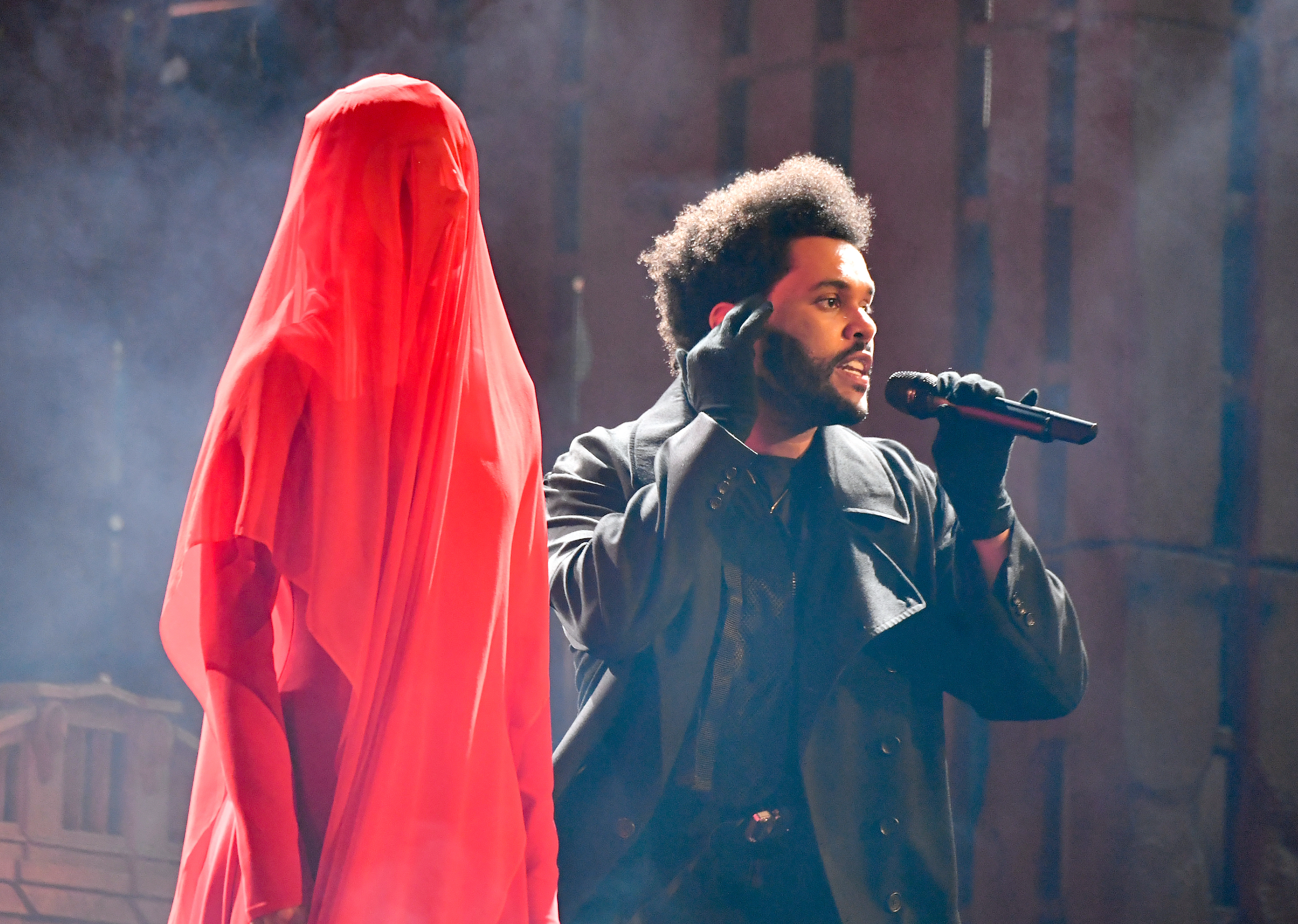The Weeknd onstage with a completely covered person standing next to him as he sings