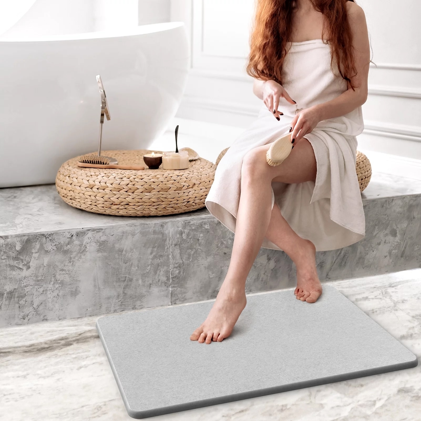 model sitting on a step next to a bath rub and stepping on a stone bath mat