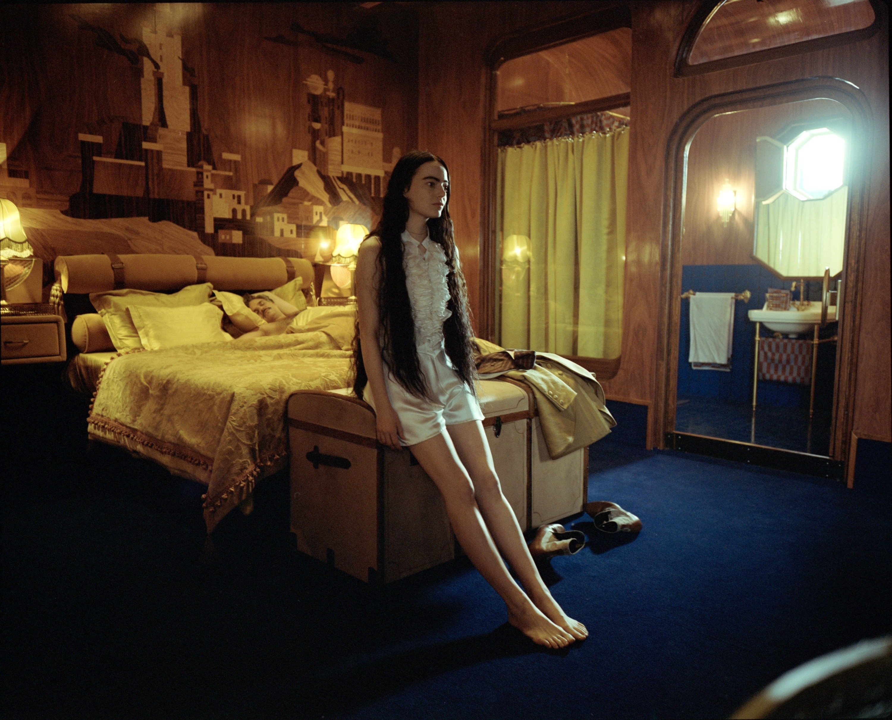 Bella sitting on a trunk in front of a bed in a scene from &quot;Poor Things&quot;